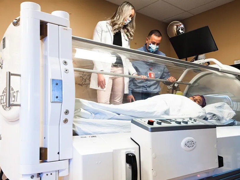 A patient lying inside a hyperbaric oxygen therapy chamber, receiving high-pressure oxygen to support wound healing. The chamber appears safe, transparent, and clinically monitored.